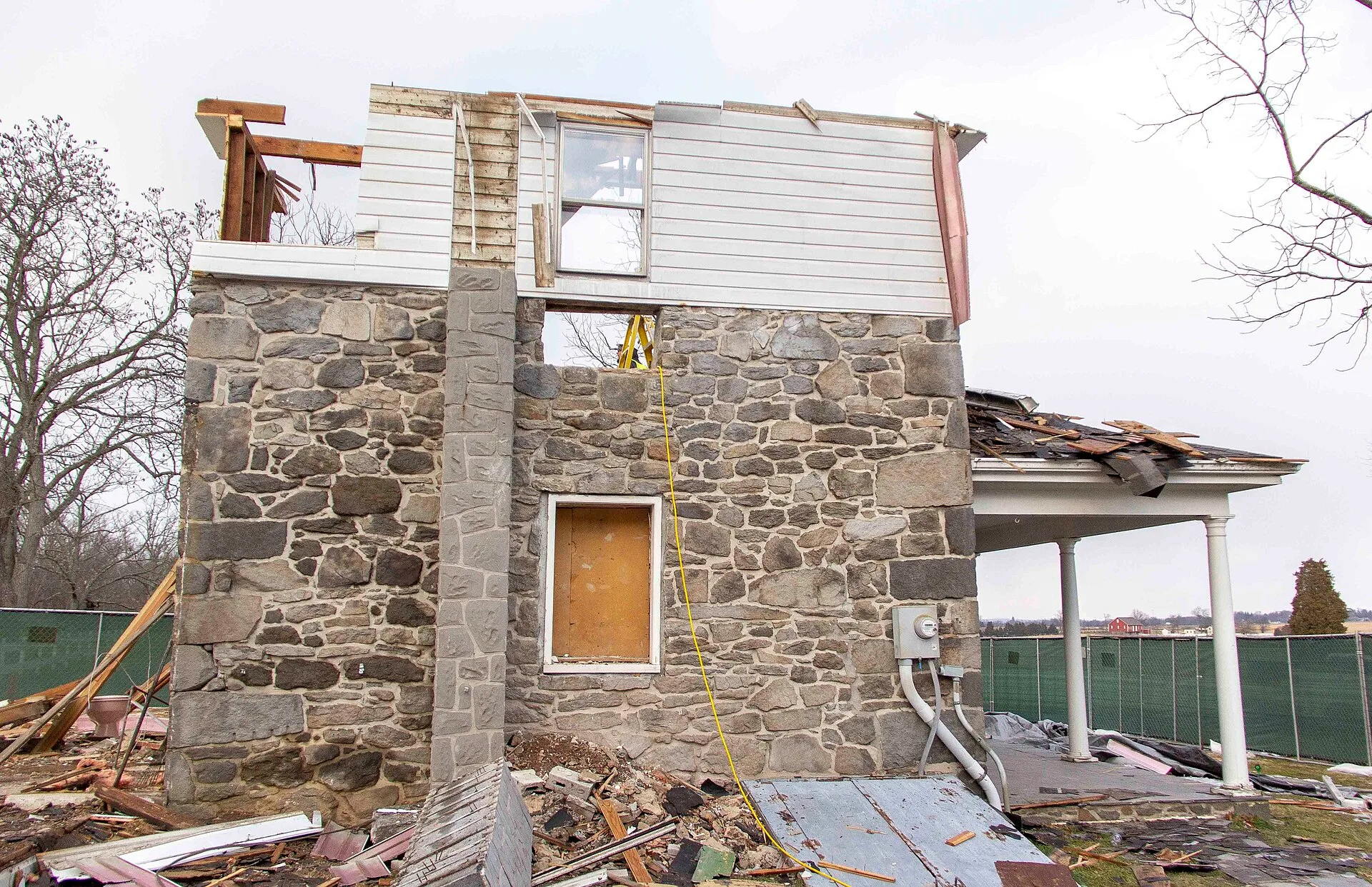 Hired contractors finish the selective demolition process on the modern additions of the house. This is a side view of the house. The repaired historic window is in the center of the original masonry structure. The second floor modern white siding remains only on this side of the house. The front po. Porch restoration contractor or board-replacer: who really restores?